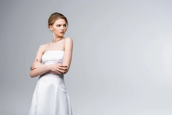 Displeased bride in white wedding dress standing with crossed arms isolated on grey — Stock Photo