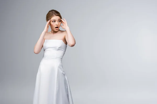 Schockiertes Mädchen im Brautkleid, das wegschaut und Schläfen berührt, isoliert auf grau — Stockfoto