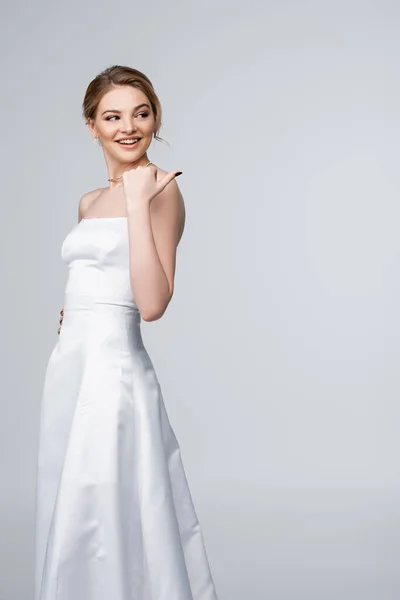 Hermosa mujer en vestido de novia blanco apuntando con el pulgar aislado en gris - foto de stock