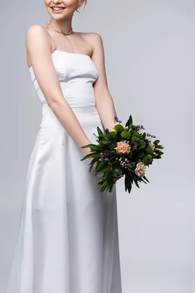 Vista cortada de noiva feliz em vestido branco segurando flores isoladas em cinza — Fotografia de Stock