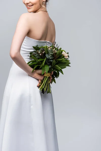 Обрезанный вид молодой и веселой женщины в белом свадебном платье проведение букет цветов изолированы на серый — стоковое фото