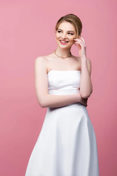 Happy bride in white wedding dress touching face isolated on pink — Stock Photo