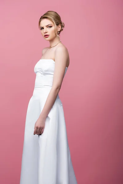 Mariée sérieuse en robe de mariée blanche regardant la caméra isolée sur rose — Photo de stock