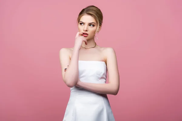 Novia pensativa en vestido de novia blanco mirando hacia otro lado aislado en rosa - foto de stock