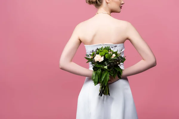 Cropped view of bride in white wedding dress holding flowers behind back isolated on pink — Stock Photo