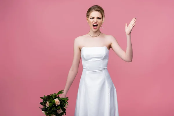 Emotionale Braut im weißen Hochzeitskleid mit Blumen, schreiend und gestikulierend isoliert auf rosa — Stockfoto
