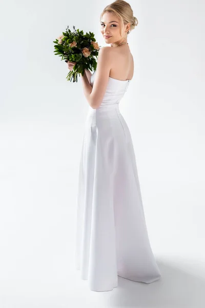 Noiva feliz em vestido de noiva elegante segurando flores no branco — Fotografia de Stock