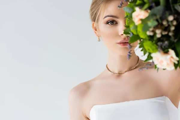 Bela noiva em elegante vestido de noiva cobrindo rosto com flores isoladas no branco — Fotografia de Stock