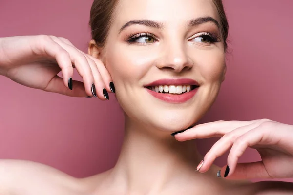 Fröhliche junge Frau mit Lidschatten und Lippenstift berührt Gesicht auf rosa — Stockfoto