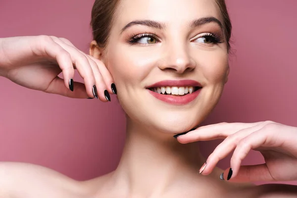 Alegre joven con sombra de ojos y lápiz labial tocando la cara en rosa - foto de stock