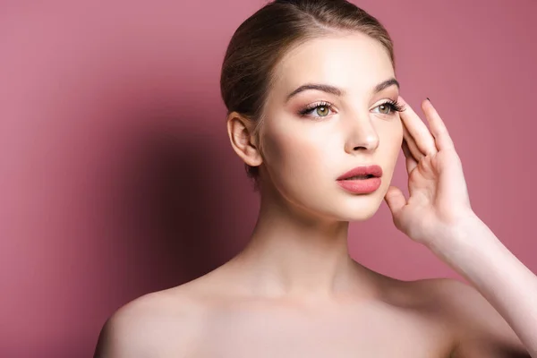 Rêveuse et nue jeune femme touchant le visage et regardant loin sur rose — Photo de stock