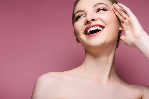 Mujer desnuda y joven con maquillaje mirando hacia otro lado y sonriendo en rosa - foto de stock