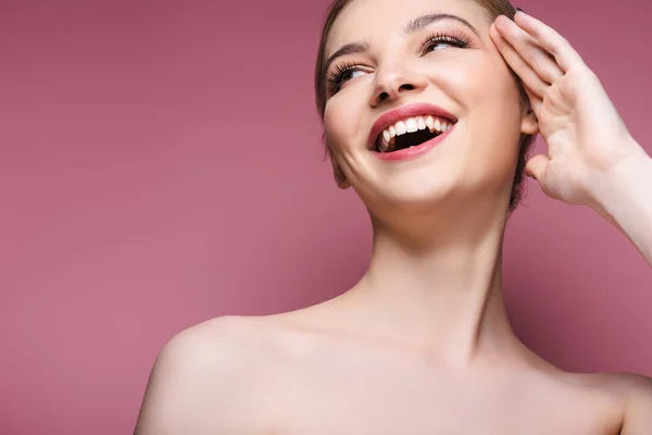 Nudo e giovane donna con il trucco guardando altrove e sorridendo sul rosa — Foto stock