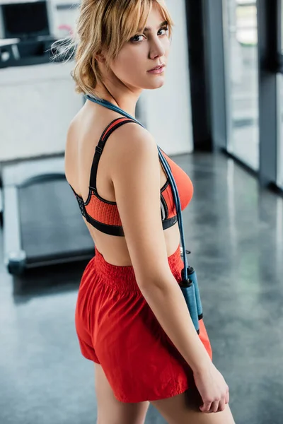 Chica atractiva en ropa deportiva de pie con saltar la cuerda y mirando a la cámara - foto de stock