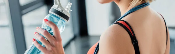 Panoramic crop of sportswoman holding sports bottle with water in gym — Stock Photo