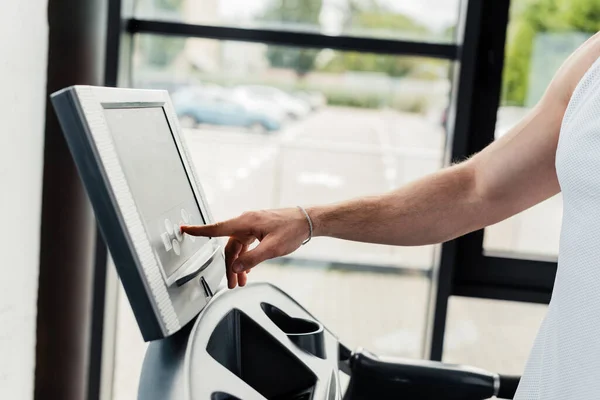 Vista recortada del deportista apuntando con el dedo a la pantalla del sensor en la cinta de correr en el gimnasio - foto de stock