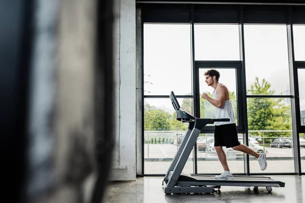 Selective focus of handsome sportsman running on treadmill in gym — Stock Photo