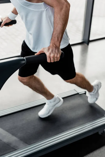 Cropped view of tired sportsman touching handrails on treadmill — Stock Photo