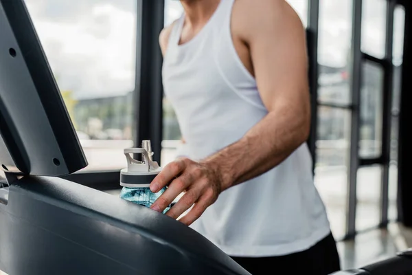 Cropped view of sportsman touching sports bottle in gym — Stock Photo