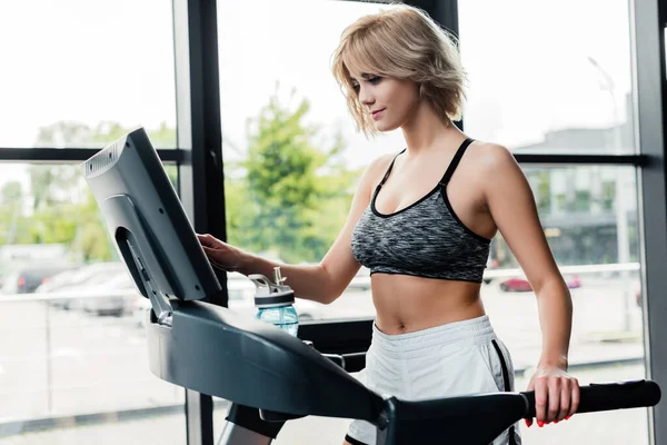 Attractive sportswoman touching screen on modern treadmill — Stock Photo