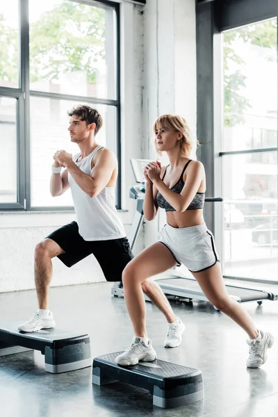 Deporte pareja con apretado manos haciendo embestidas ejercicio en paso plataformas - foto de stock