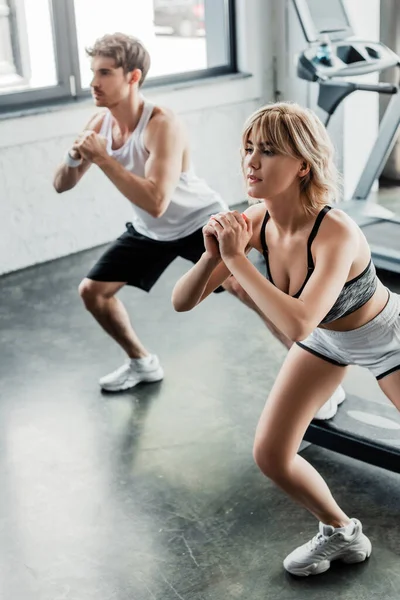 Enfoque selectivo de la pareja de jóvenes deportistas haciendo ejercicio en el gimnasio - foto de stock