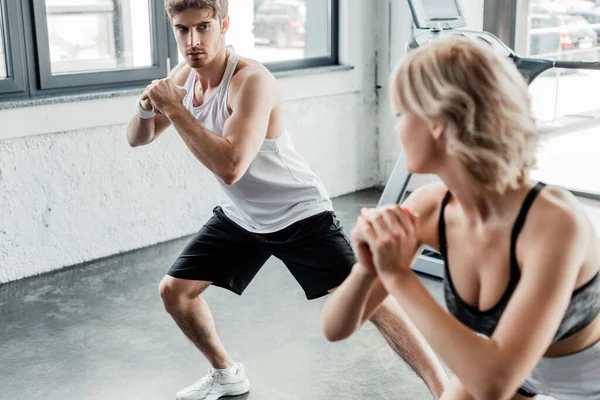 Selective focus of young sport couple with clenched hands looking at each other and exercising in gym — Stock Photo