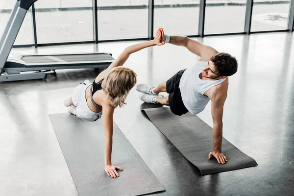 Desportista feliz e atraente desportista dando alta cinco enquanto se exercita em tapetes de fitness — Fotografia de Stock