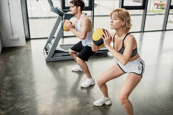 Bello e sportivo uomo esercizio con palla vicino attraente ragazza in palestra — Foto stock