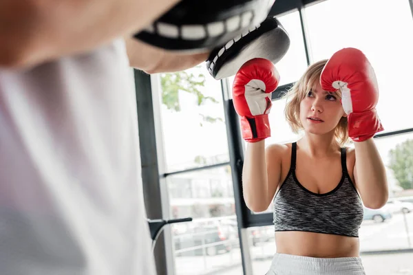 Selective focus of sportive woman in boxing gloves exercising with man in boxing pads — Stock Photo
