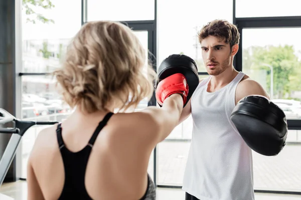 Back view of sportive woman in boxing gloves exercising with man in boxing pads — Stock Photo