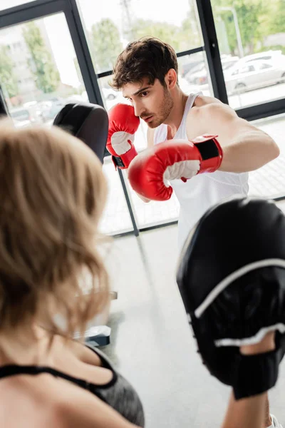 Selective focus of sport couple in boxing gloves and boxing pads training in gym — Stock Photo