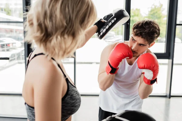 Selective focus of sportsman in boxing gloves exercising with girl in gym — Stock Photo