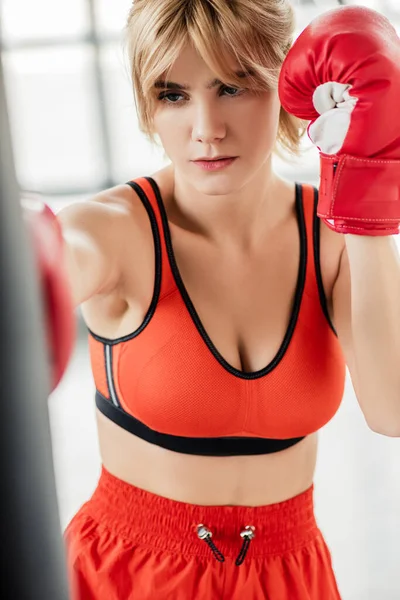 Selective focus of sportswoman in boxing gloves exercising with punching bag — Stock Photo