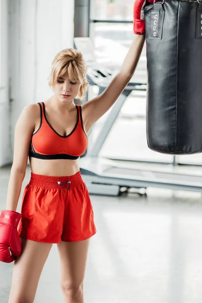 Tired sportswoman in boxing gloves standing near punching bag — Stock Photo
