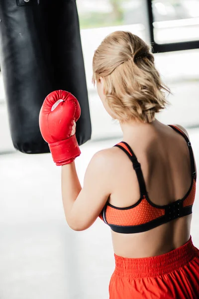 Вид сзади спортивной девушки в боксерских перчатках с проколотой сумкой — стоковое фото