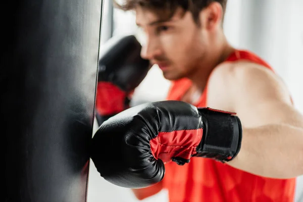 Foco seletivo do boxeador atlético em luvas de boxe trabalhando com saco de perfuração — Fotografia de Stock