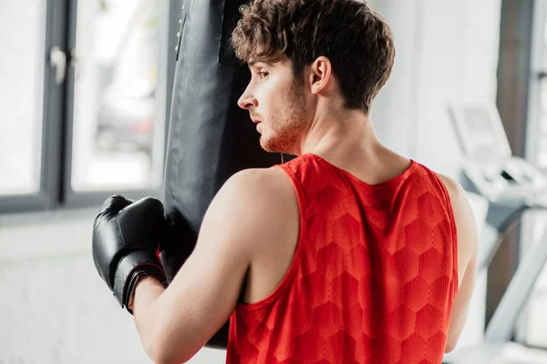 Müder Mann in Sportbekleidung und Boxhandschuh berührt Boxsack in Turnhalle — Stockfoto
