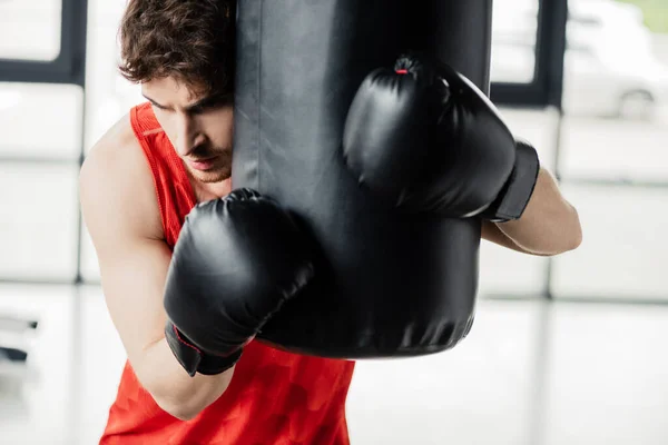 Uomo stanco in abbigliamento sportivo e guanti da boxe neri toccare sacco da boxe in palestra — Foto stock