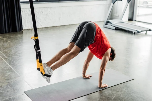 Homme athlétique en vêtements de sport faisant de l'exercice avec des bandes de résistance sur tapis de fitness — Photo de stock