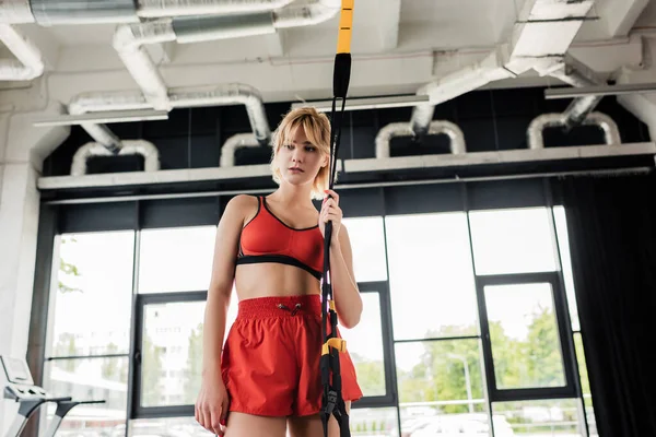 Tired sportswoman standing and touching resistance bands in gym — Stock Photo