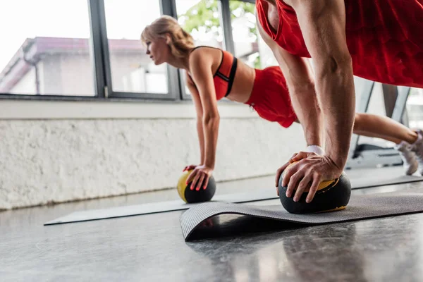 Messa a fuoco selettiva dello sportivo che si esercita con la palla sul tappeto fitness vicino alla ragazza — Foto stock