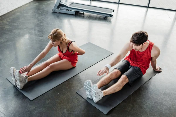 Visão de alto ângulo do casal esporte em sportswear alongamento em tapetes de fitness no ginásio — Fotografia de Stock