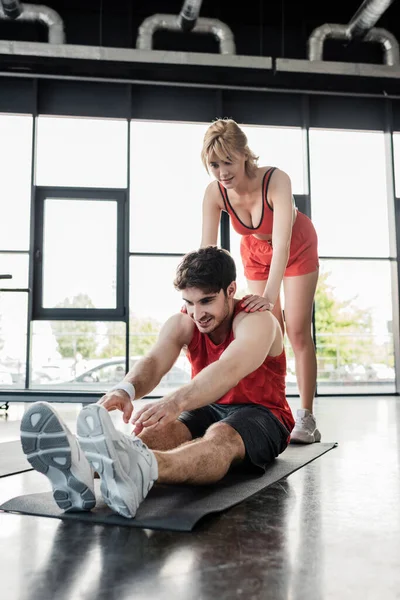 Beautiful woman touching happy sportsman stretching on fitness mat — Stock Photo