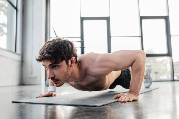 Shirtless sportsman doing push ups on fitness mat in gym — Stock Photo