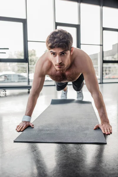 Deportista sin camisa haciendo ejercicio en la alfombra de fitness en el gimnasio - foto de stock