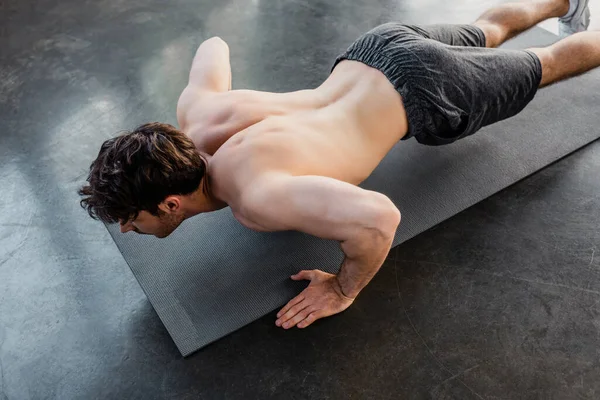 Overhead view of shirtless sportsman doing push ups on fitness mat in gym — Stock Photo