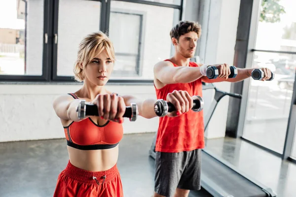 Enfoque selectivo de la pareja deportiva haciendo ejercicio con pesas en el gimnasio - foto de stock