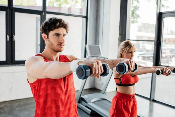 Selective focus of man and woman working out with dumbbells in gym — Stock Photo