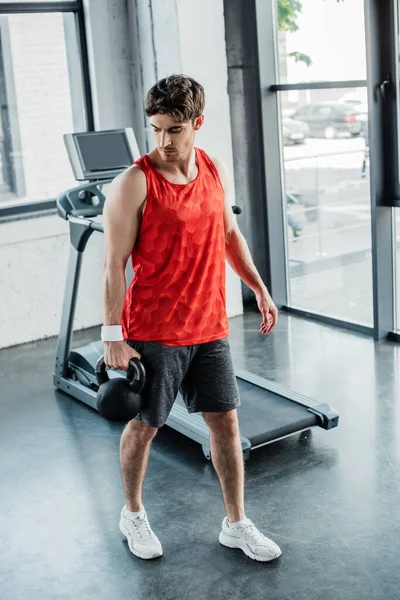 Strong man holding heavy dumbbell near treadmill in sports center — Stock Photo